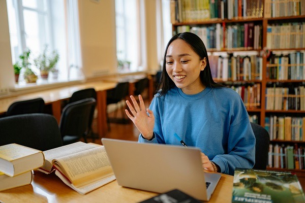 A student sitting in library with a lots of books in the background . she appears to be engaged in an online calculus session for her homework and assignment