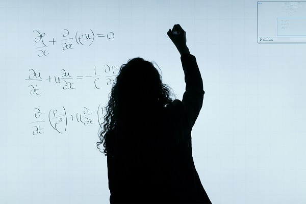 A woman with long curly hair meticulously writes complex differential equations on a whiteboard, focusing on partial derivatives and fluid dynamics.