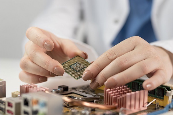 A student of semiconductor in a white lab coat carefully places a computer processor onto a motherboard. The hands are shown holding the semiconductor chip above the socket, surrounded by various electronic components. The scene highlights precision in computer hardware assembly. the image illustrate the concept of semiconductor physics assignment help