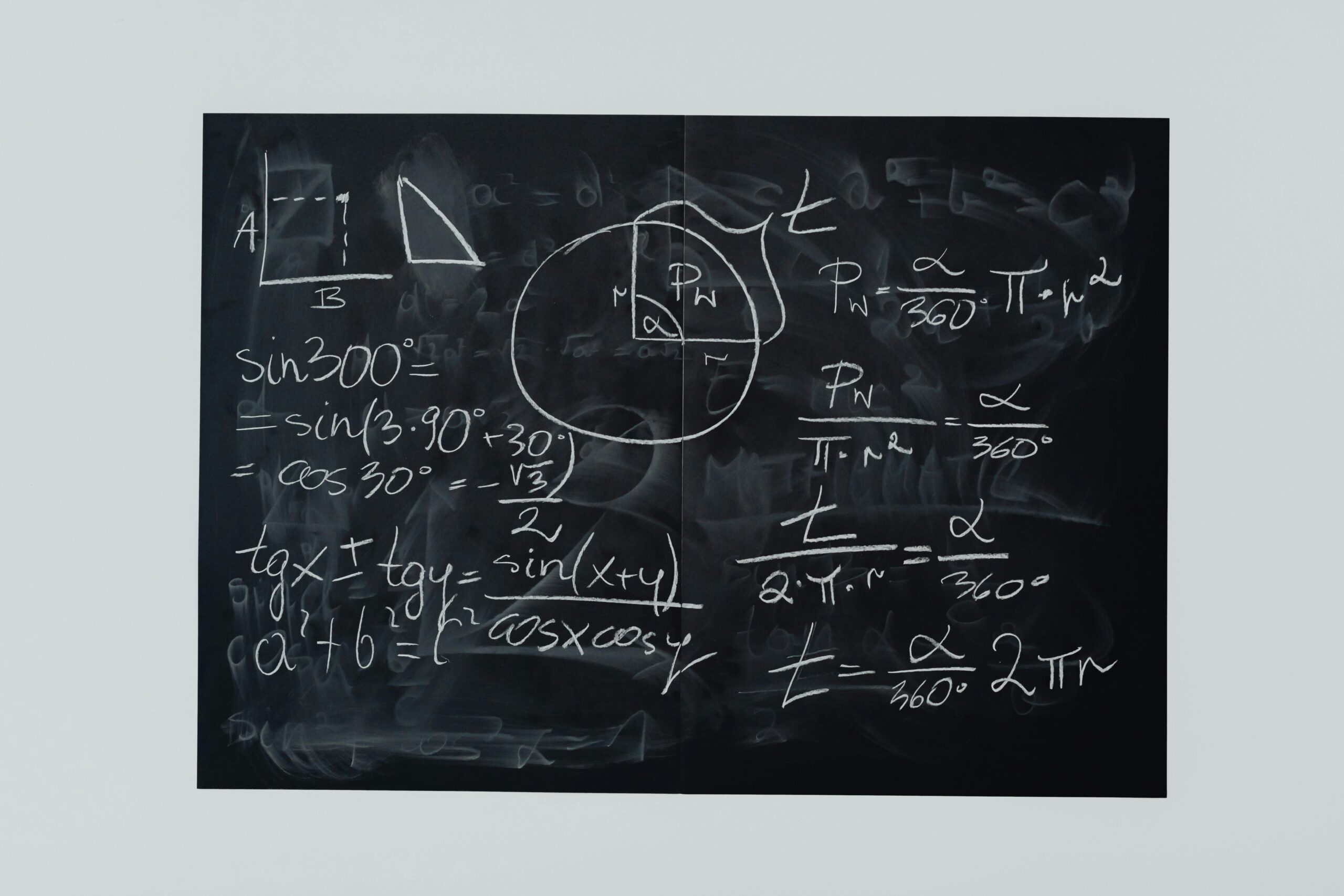 A chalkboard with various mathematical equations and diagrams. The board features trigonometry equations, geometric shapes, and a circle with markings, illustrating mathematical concepts. The detailed chalk writing is partially smudged, revealing the depth of thought behind each equation