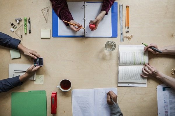 Overhead view of students collaborating at a desk with architectural homework and assignments