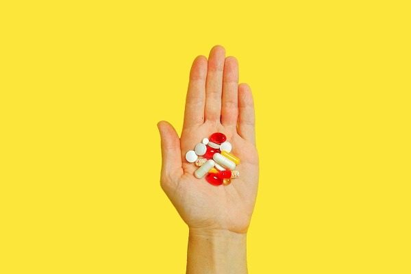 A pharmacology student's hand is shown against a bright yellow background, holding a variety of pills and capsules of different colors and sizes indiacates the conept of pharmacology assignment help